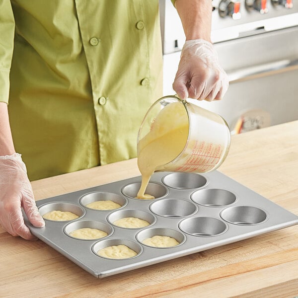 A person pouring batter into a Baker's Mark jumbo muffin pan.