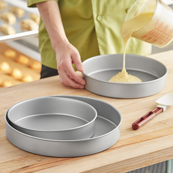 A woman pouring yellow cake batter into a Baker's Mark round cake pan.
