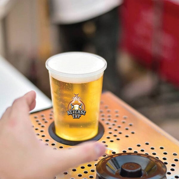 A hand pressing a ReverseTap cup of beer on a metal table.