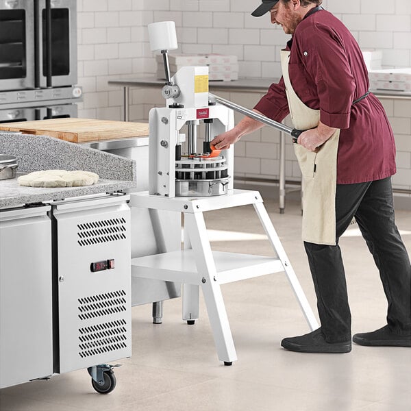 A man in a chef's hat and apron using an Estella manual dough divider to portion pizza dough on a counter.