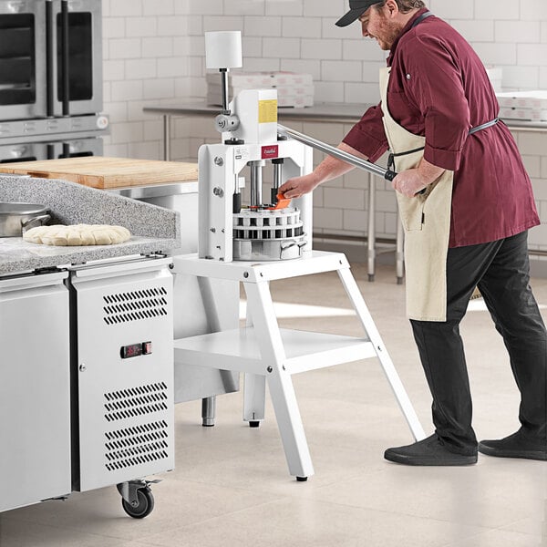 A man in a chef's hat using an Estella Manual Dough Divider in a professional kitchen.