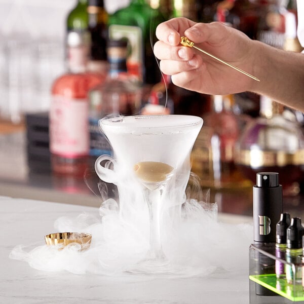 A hand using a Flavour Blaster Mini to add smoke to a martini glass.