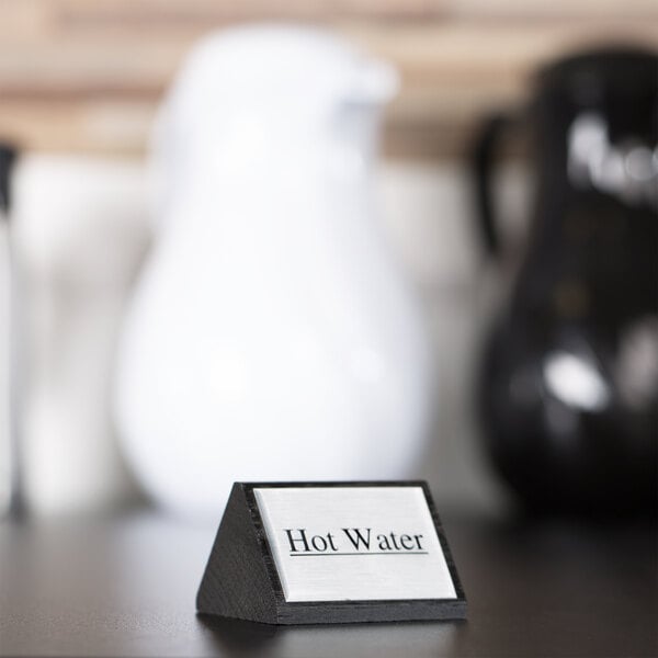 A close-up of a black wood American Metalcraft "Hot Water" sign on a table.