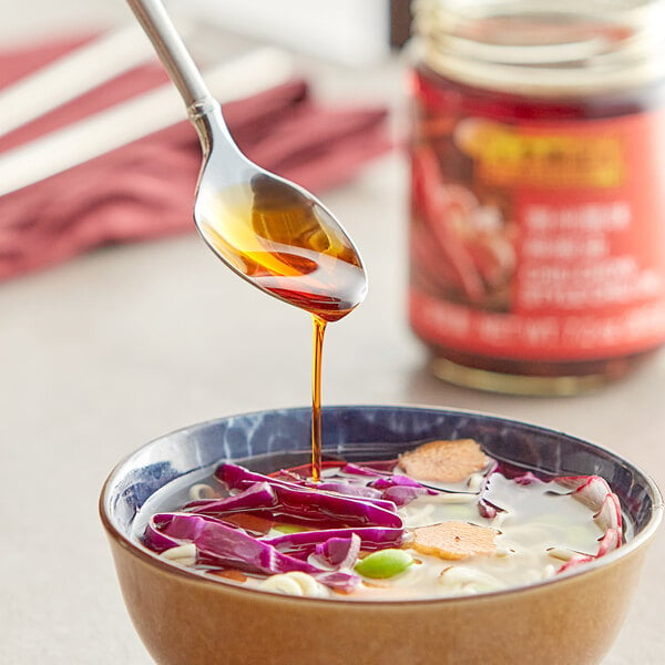 A spoon pouring Lee Kum Kee Chiu Chow Chili Oil into a bowl of soup.