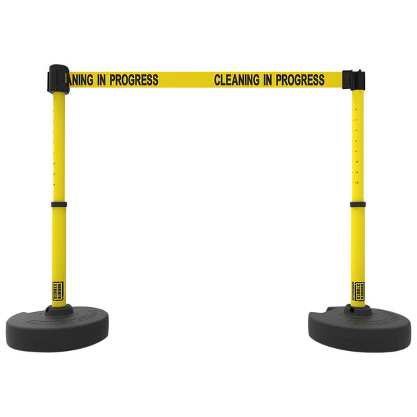 Two yellow and black Banner Stakes poles with a "Cleaning in Progress" sign.