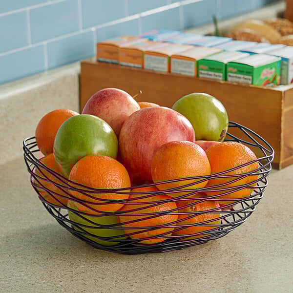 A Tablecraft black wire square basket filled with oranges and a green apple.