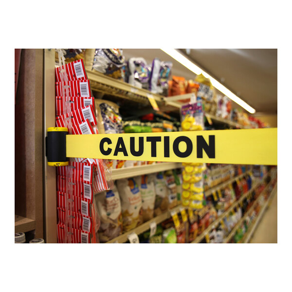 A yellow Banner Stakes "Caution" tape on a grocery store shelf.