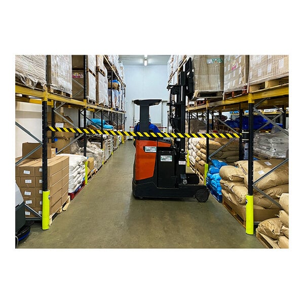 A yellow and black Banner Stakes wall mount barrier attached to a forklift in a warehouse.