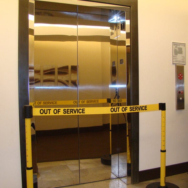 A glass elevator door with yellow "Out of Service" caution tape.