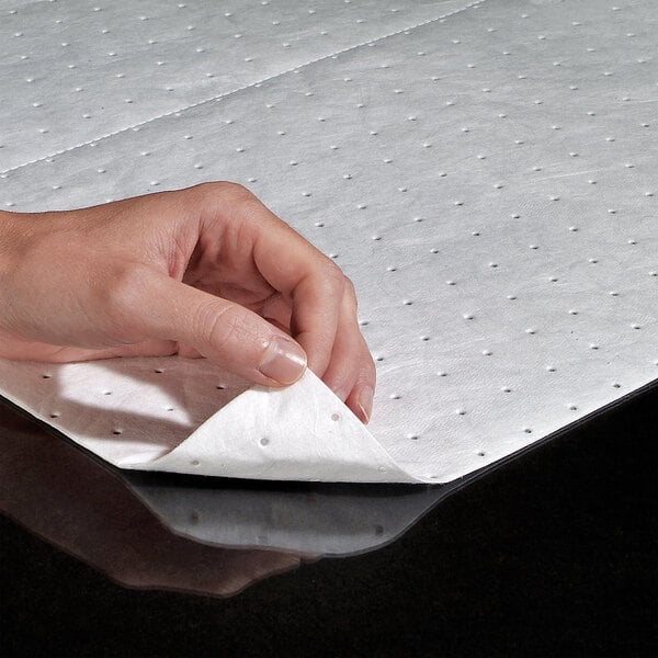 A white, perforated absorbent mat pad being lifted by a hand, designed for oil-based liquid spills.