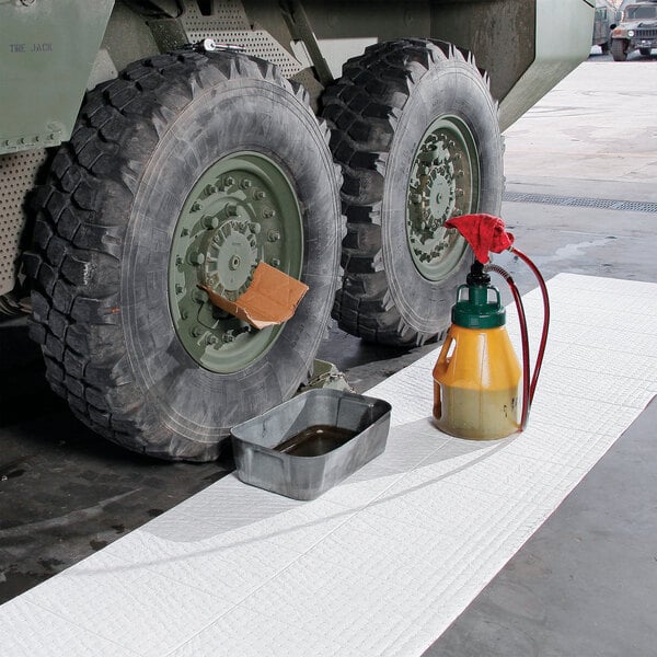 A white absorbent mat roll designed for oil-based liquids, shown placed under a vehicle with maintenance equipment.