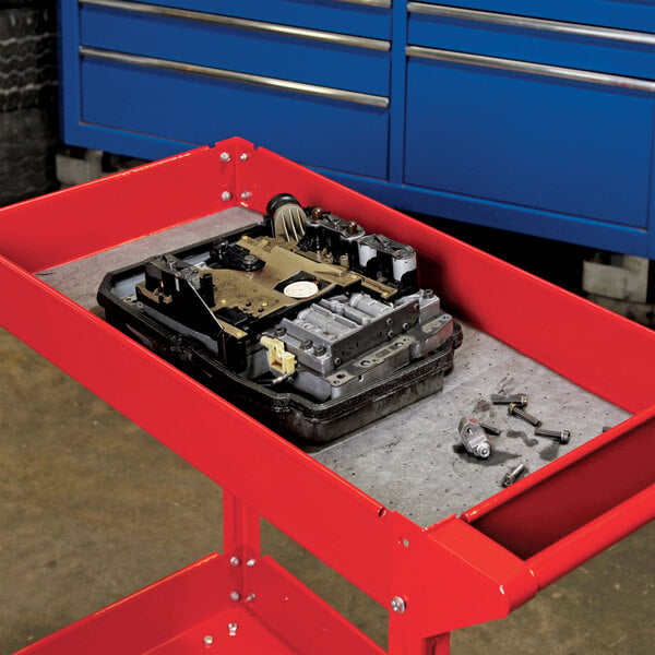 A gray absorbent mat roll placed on a red utility cart, used for soaking up spills in industrial or automotive settings.