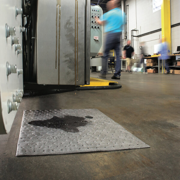 A gray absorbent mat pad placed on an industrial floor to soak up liquid spills.
