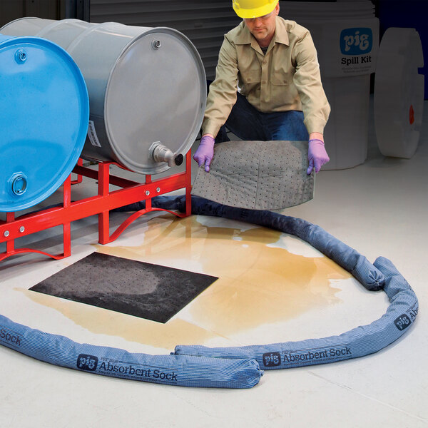 A blue absorbent sock used for containing and cleaning up liquid spills, shown encircling a spill near industrial drums.