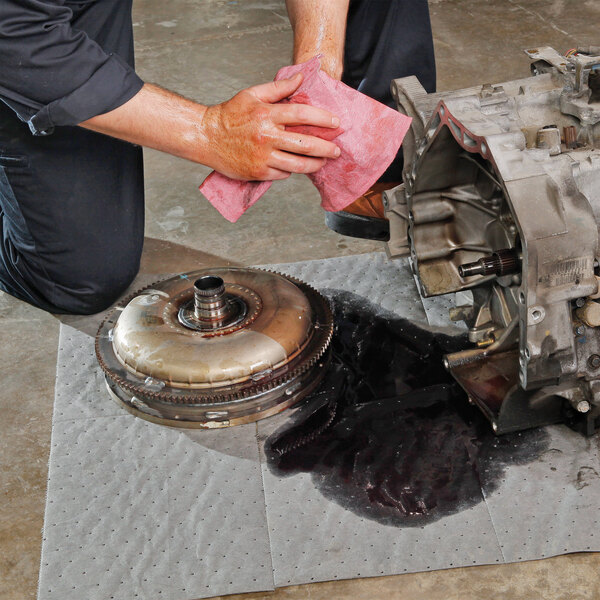 A medium weight absorbent mat roll being used to soak up spilled oil under automotive parts.