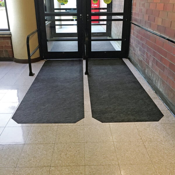 A long black adhesive-backed floor mat placed at the entrance of a building.