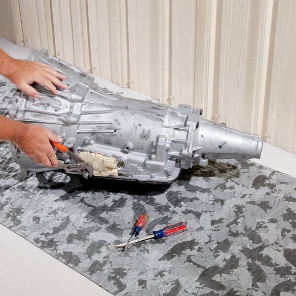 A gray camouflage absorbent heavy weight mat roll being used as a work surface under a transmission and tools.