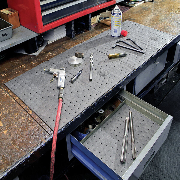 A heavy weight absorbent mat roll used for protecting work surfaces from spills and leaks in industrial or workshop settings.