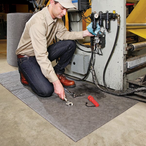 A large gray absorbent mat roll placed on the floor under machinery to catch spills and drips.