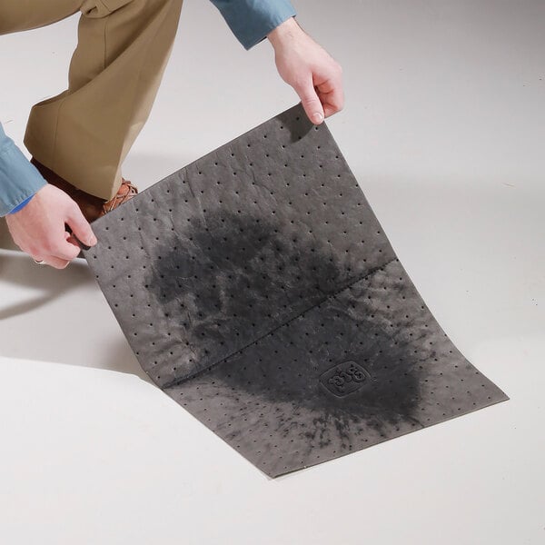 A black absorbent medium weight mat pad being held by a person, showing a large wet spot in the center.