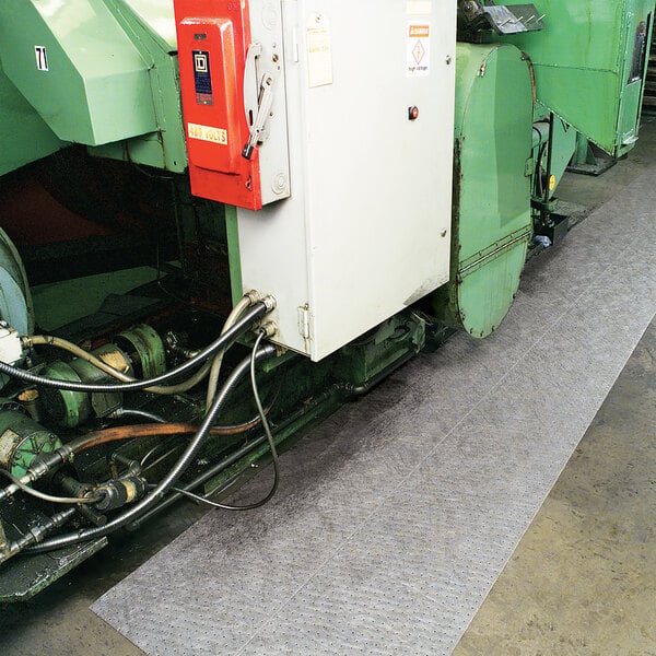 A long, gray absorbent mat roll placed on the floor next to industrial machinery.
