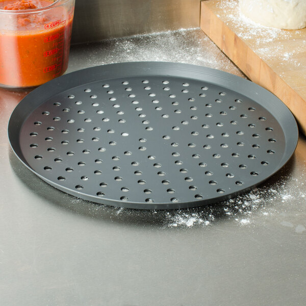 An American Metalcraft perforated hard coat anodized aluminum pizza pan on a counter.