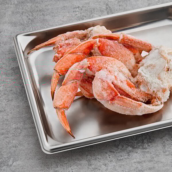 A cluster of frozen Dungeness crab legs on a stainless steel tray.