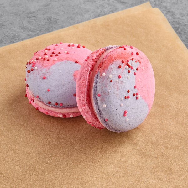 Two Macaron Centrale raspberry caramel macarons on a piece of paper.