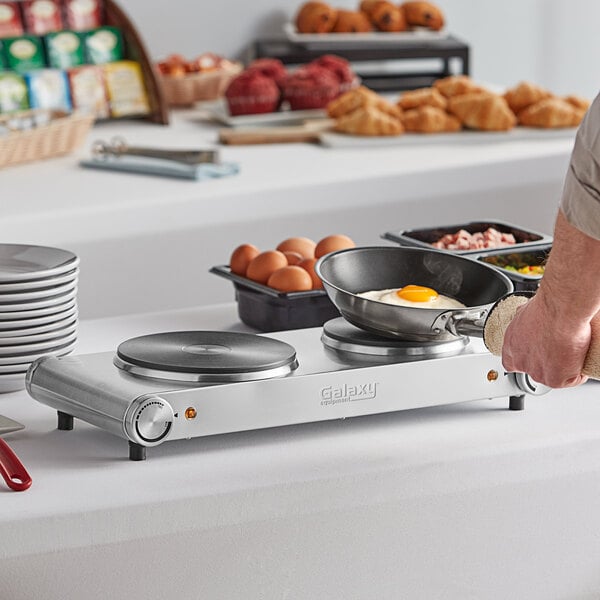 A person cooking fried eggs on a Galaxy double burner hot plate.