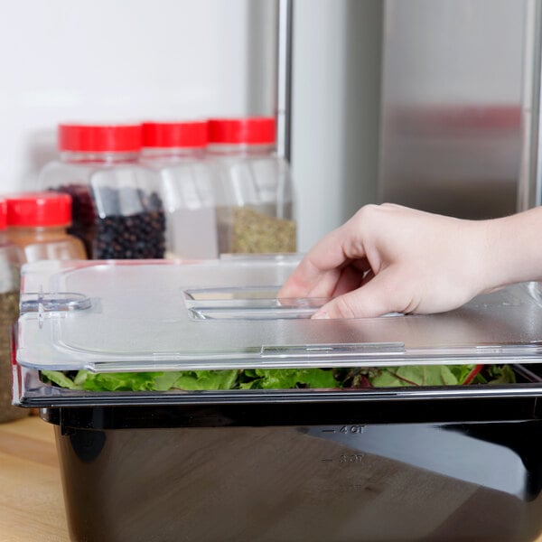 A hand opening a Carlisle plastic container of salad with a leafy vegetable.