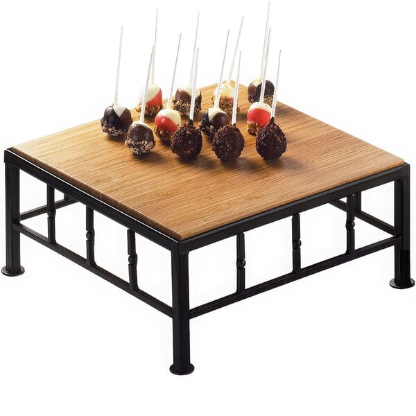 A Cal-Mil iron black square riser with a bamboo top on a wooden table with chocolate balls on it.