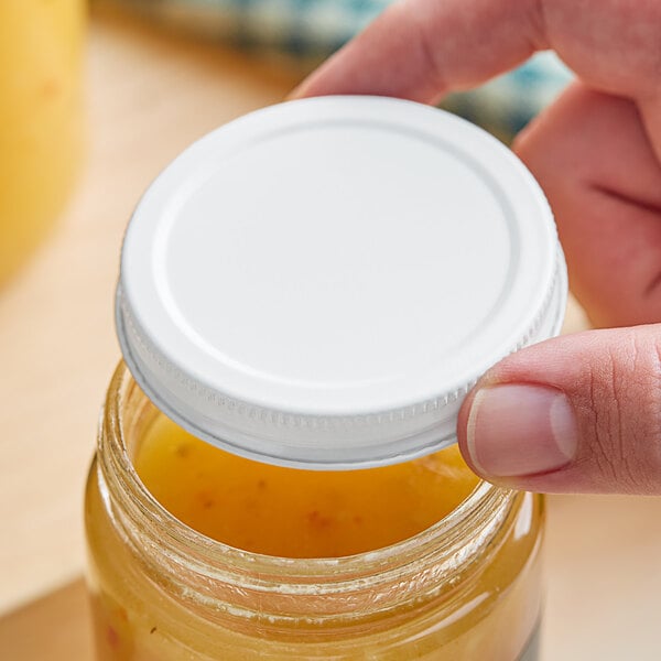 A hand holding a white metal lid over a jar.