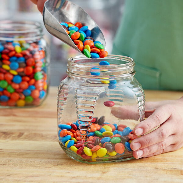 A hand pouring candy into a Square Glass Honey Jar.