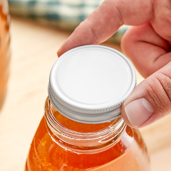 A hand holding a jar with a white metal lid containing orange liquid.