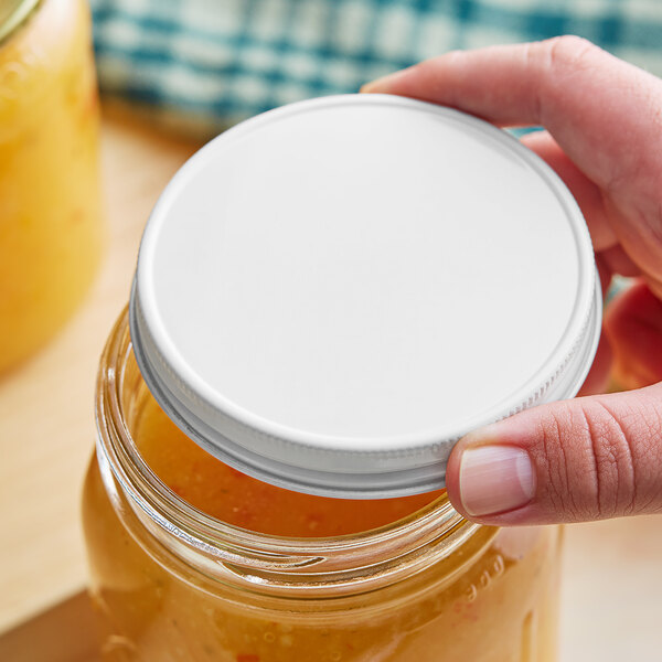 A hand holding a white 89/400 metal lid over a jar of yellow liquid.