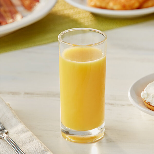 A glass of Ocean Spray orange juice on a table next to a plate of food.