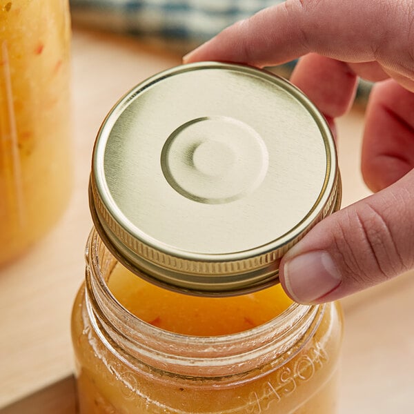 A hand holding a 70/450 gold metal lid over a jar of yellow liquid.