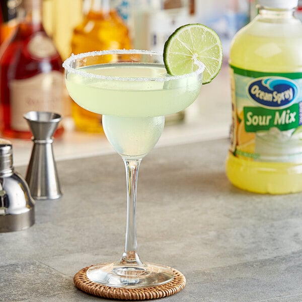 A glass with a drink made with Ocean Spray Sour Mix and a lime wedge on the rim.