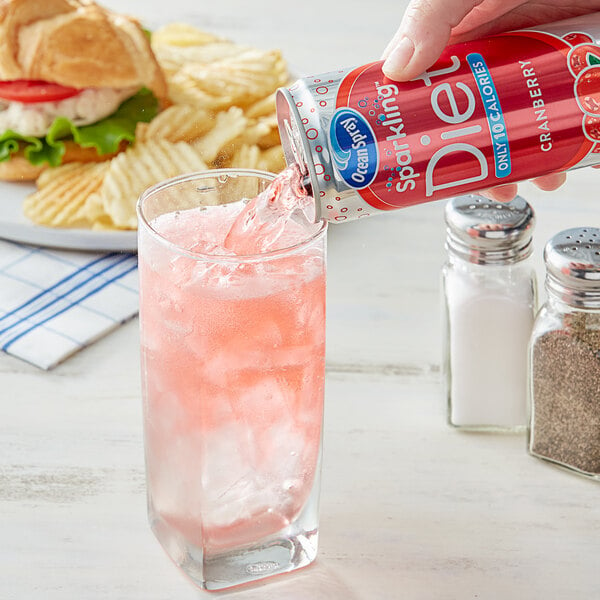 A hand pouring Ocean Spray Diet Sparkling Cranberry Juice into a glass of ice.