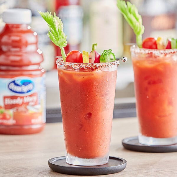 Two Bloody Mary cocktails in glasses on a table with a bottle of Ocean Spray Bloody Mary Mix.