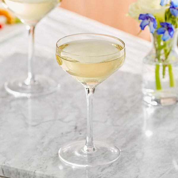 Two Acopa Silhouette coupe glasses of white wine on a marble table.