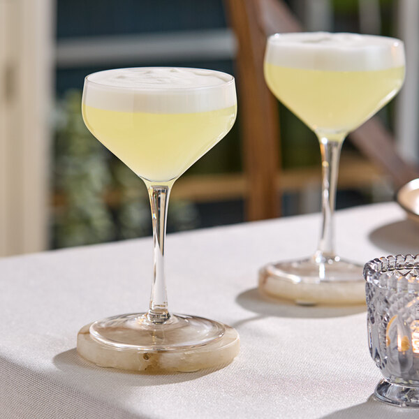 Two Acopa Silhouette coupe glasses filled with yellow liquid on a table.