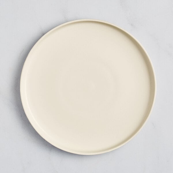 An Acopa Pangea fog white matte coupe porcelain plate on a marble surface.