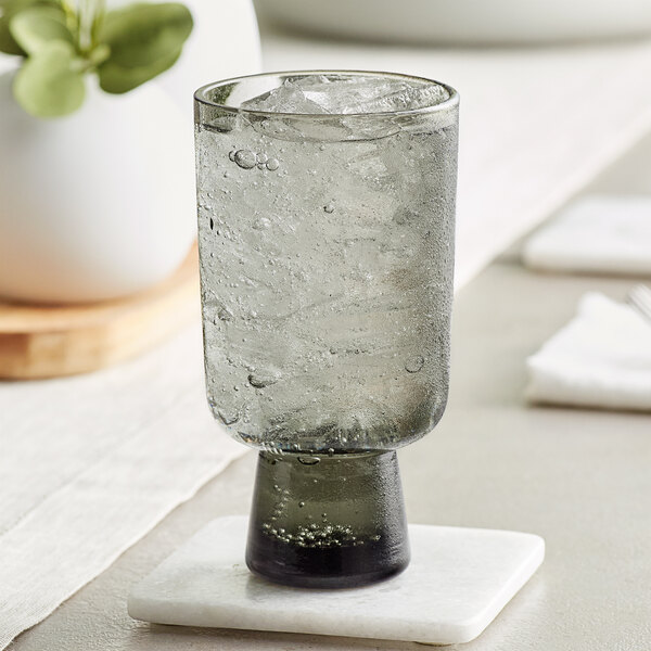 An Acopa Pangea gray goblet with ice water on a white marble coaster.