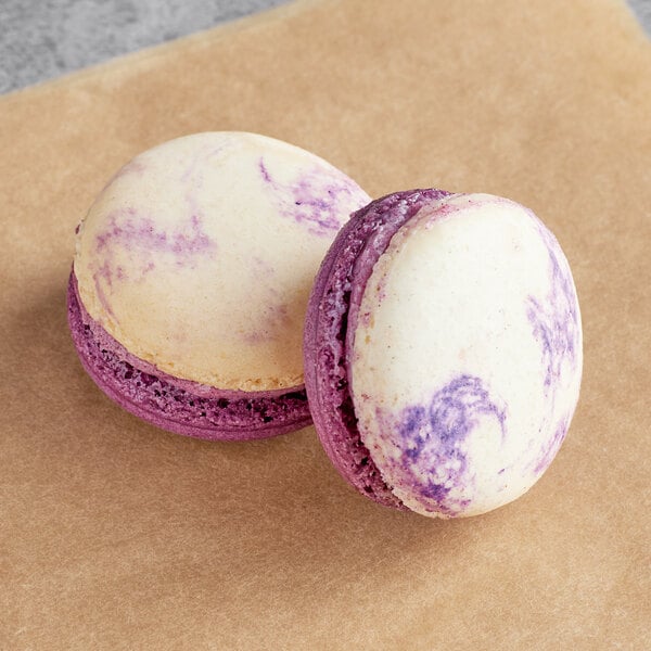 Two Ube white chocolate macarons with purple and white shells on a table.