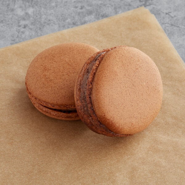 Two Macaron Centrale vegan chocolate macarons on a brown surface.