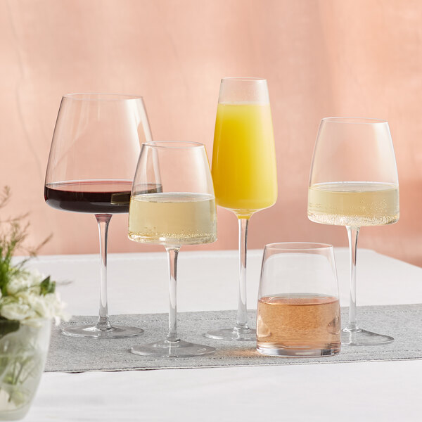 A table with four Acopa Piatta white wine glasses and a glass of yellow liquid.