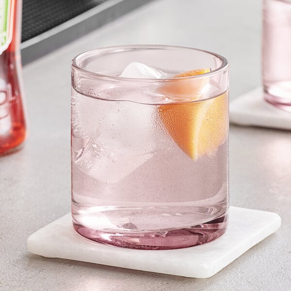 A Mauve Acopa Pangea rocks glass with water, ice, and an orange slice on a table.