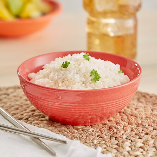 An Acopa Capri coral stoneware nappie bowl filled with rice sits on a table next to a pair of chopsticks.