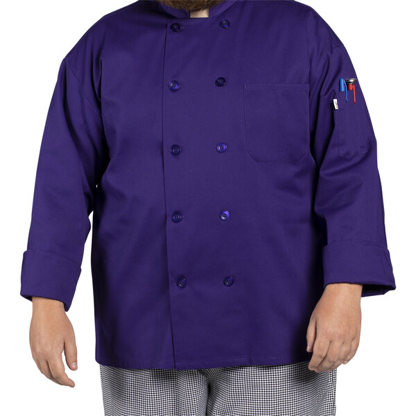 A man wearing a purple Uncommon Chef long sleeve chef coat on a counter in a professional kitchen.